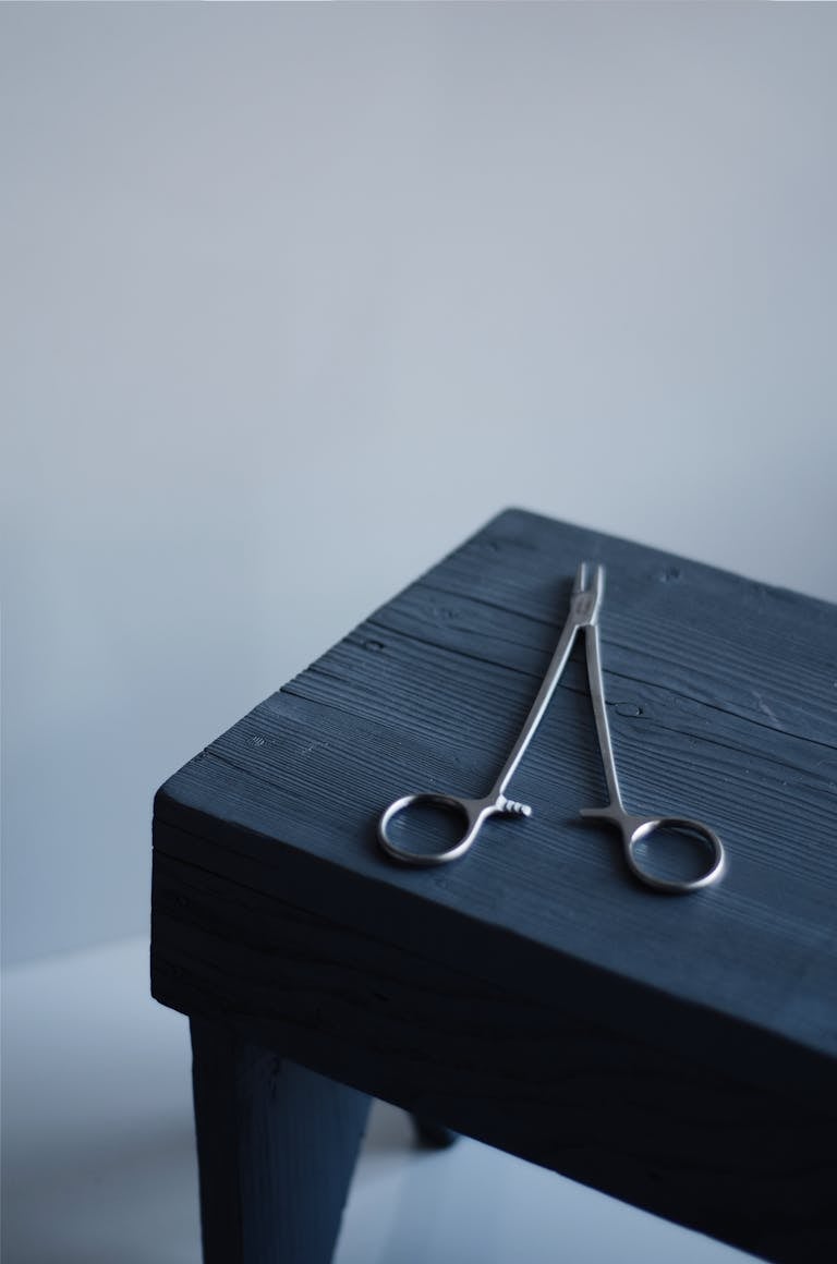 A pair of steel surgical scissors placed on a dark wooden table with a minimalist background.
