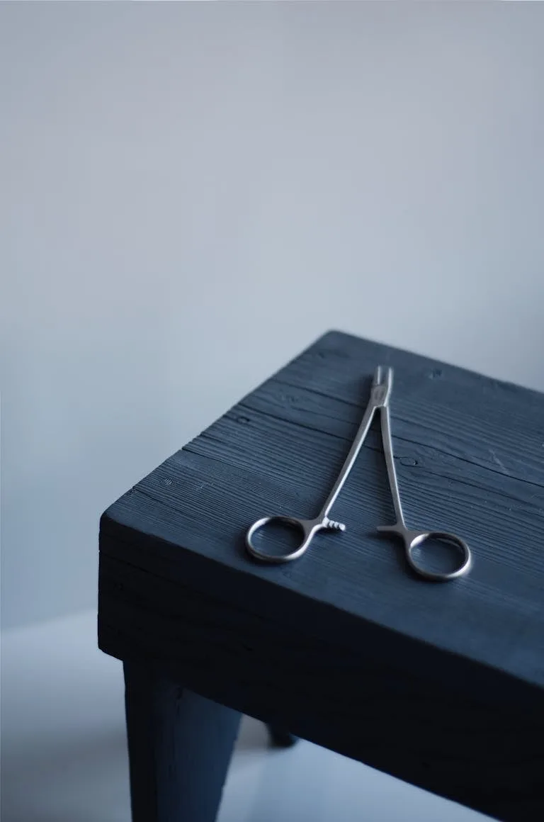 A pair of steel surgical scissors placed on a dark wooden table with a minimalist background.