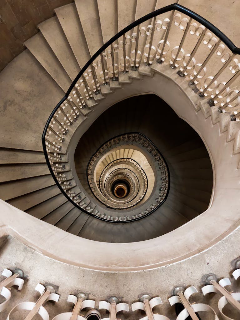 Vertigo-inducing view of a spiral staircase with ornate railings seen from above indoors.